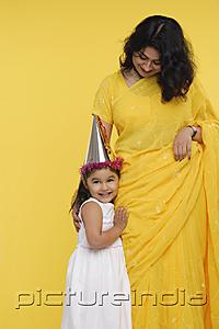 PictureIndia - Young girl in white dress and party hat, standing next to her mother