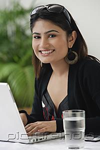 PictureIndia - Woman using laptop, smiling at camera